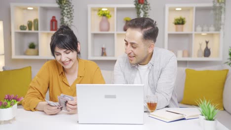 couple counting money while looking at laptop.