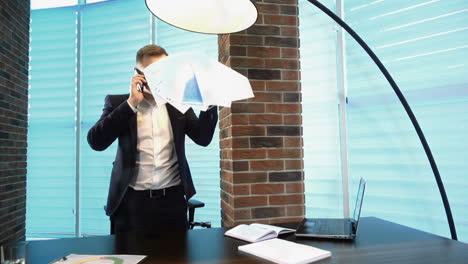 a businessman talking on a mobile phone. businessman talking on the phone and throwing paper sheets