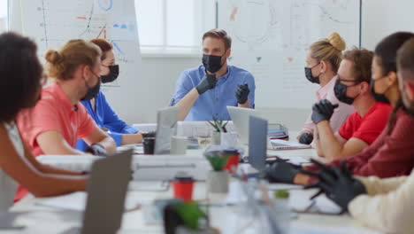 Maskierte-Menschen-Sitzen-Am-Tisch-Im-Büro.-Chef-Bespricht-Team-Drinnen.