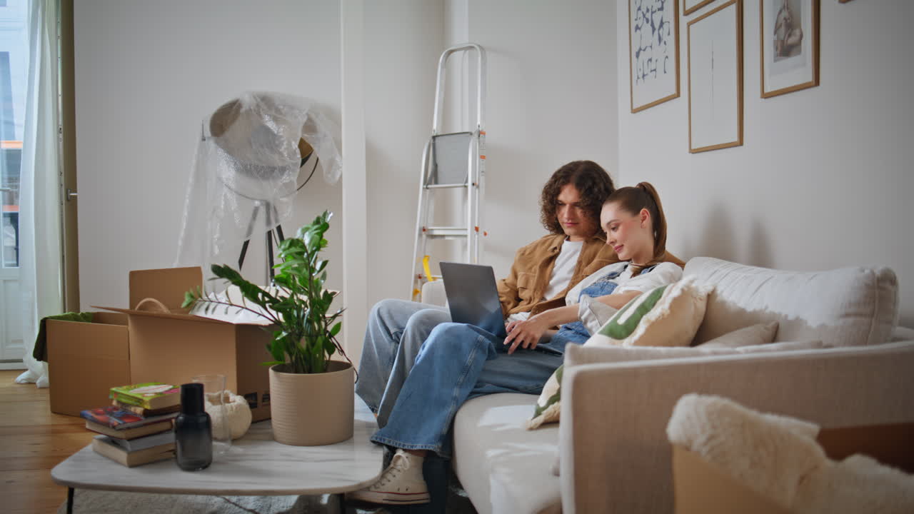 Married couple using laptop in new home feeling relaxed. Casual man and woman