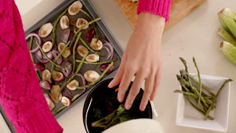 Mid-section-of-biracial-woman-putting-waste-into-bin-in-kitchen-at-home-with-copy-space,-slow-motion