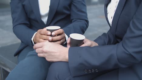 close up of two unrecognizable businesswomen drinking coffee and talking during break outside