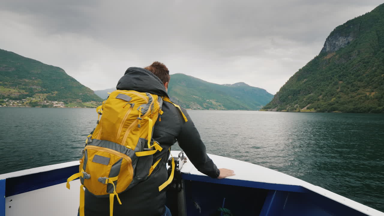 A Man With A Backpack Travels Through A Picturesque Fjord In Norway Standing On The Bow Of The Ship 