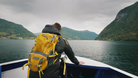 Ein-Mann-Mit-Rucksack-Reist-Durch-Einen-Malerischen-Fjord-In-Norwegen,-Der-Am-Bug-Des-Schiffes-Steht