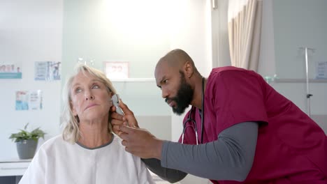 Afroamerikanischer-Arzt-Mit-Otoskop,-Der-Das-Ohr-Einer-Kaukasischen-Patientin-Im-Krankenhaus-Untersucht