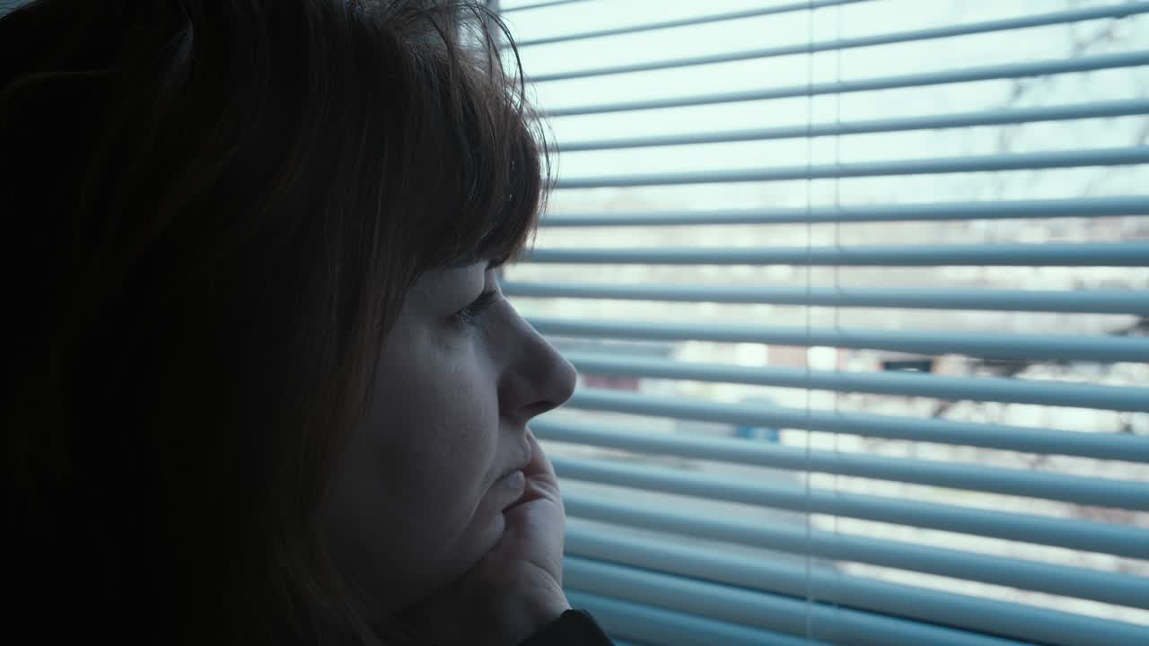 조심스러운 중년 여성이 창밖을 바라보고, 누군가를 기다리며 주위를 둘러보고 있습니다.