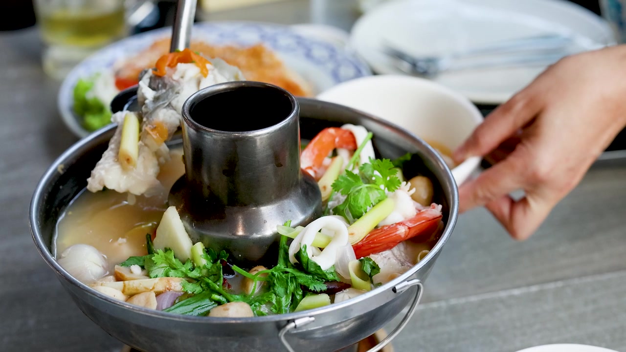 Henkilö tarjoilee thaimaalaista mausteista mereneläväkeittoa kuumasta padasta