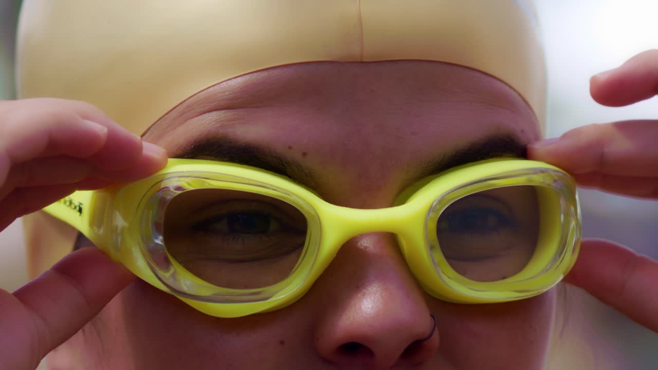 Attractive female Hispanic swimmer puts on her goggles to prepare to swim