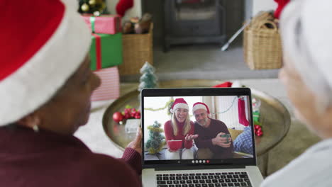 diversas amigas mayores que usan una computadora portátil para una videollamada de navidad con una pareja en la pantalla