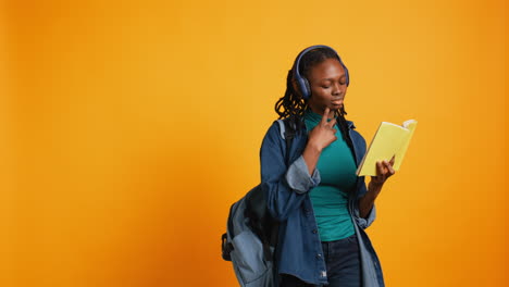 Young-girl-wearing-headphones-reading-interesting-book,-studio-background