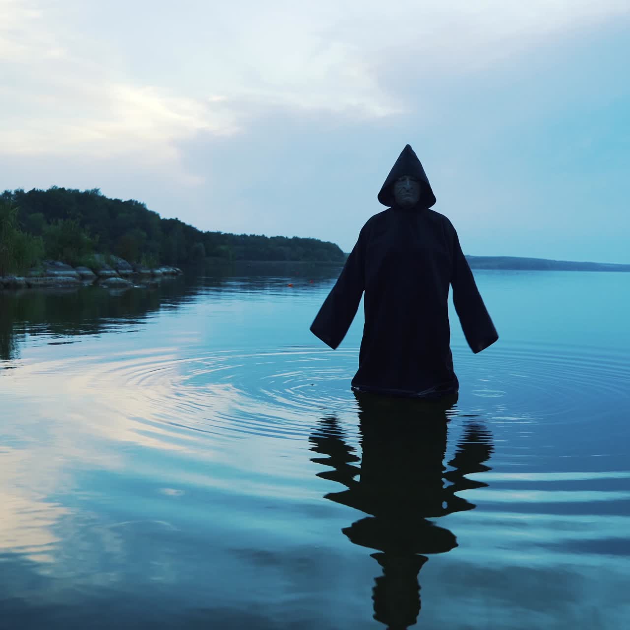 Evil witch in black cloak with hood in the river. Halloween costume.