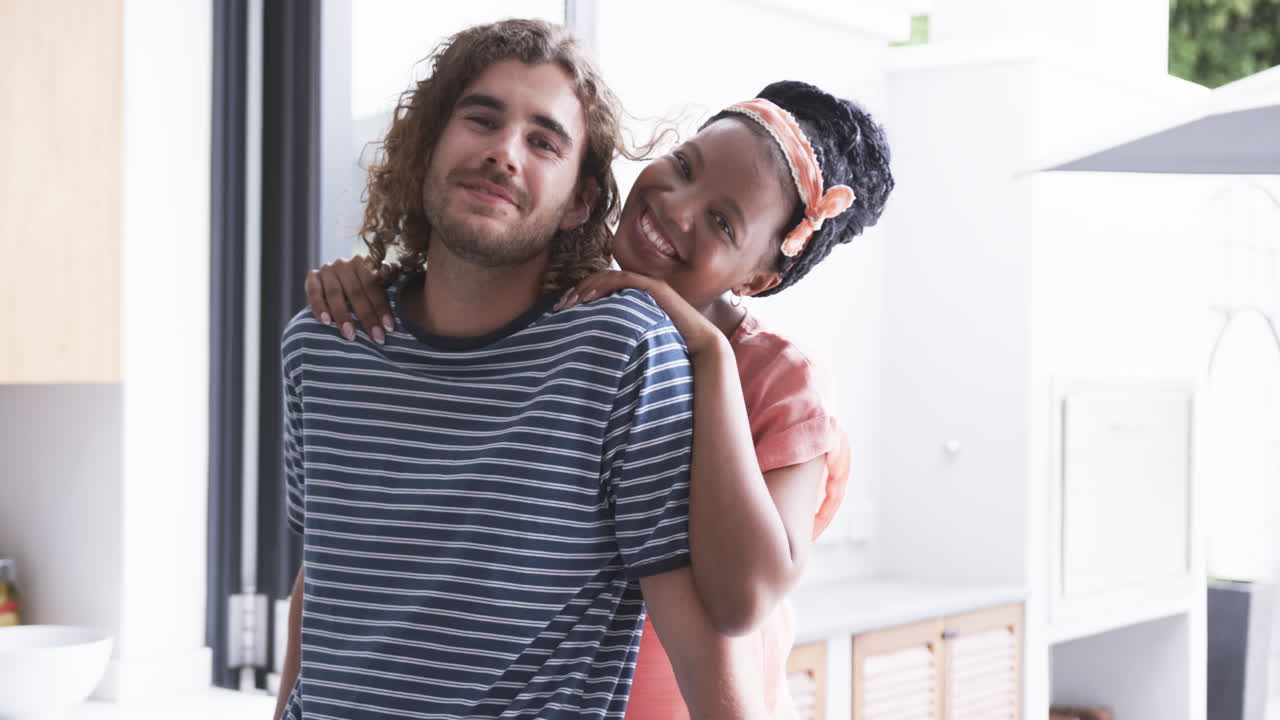 una pareja diversa sonríe cálidamente en una cocina de casa brillante