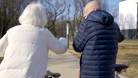 rear view of a senior couple holding bikes while walking and talking in the park on a winter day