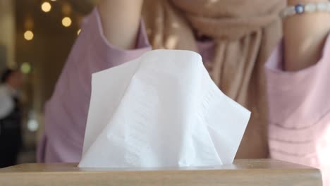 a woman pulls a tissue from a box on a table