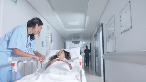 diverse female doctor and child patient talking in corridor at hospital, in slow motion