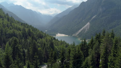 Drohnenaufnahme-Von-Zwei-Personen,-Die-Auf-Einem-Verlassenen-Gebäude-Vor-Einer-Wunderschönen-Landschaft-Mit-Großen-Bergen-Und-Einem-See-Stehen