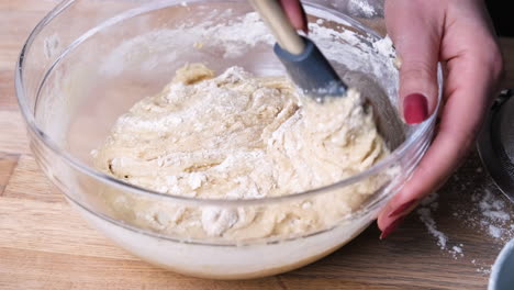 hands mixing cake batter with a spatula in a glass bowl