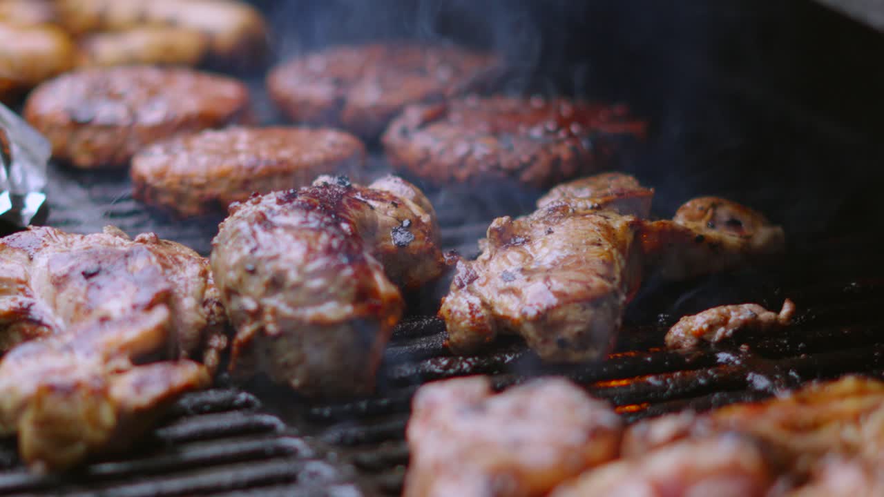 deliciosa escena general de barbacoa cocinando carne de cerdo y cordero con hamburguesas en el fondo con llamas y humo en cámara lenta 4k