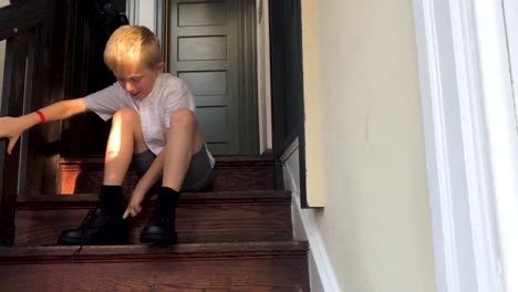 Boy-is-tying-shoes-before-school,-sitting-on-steps