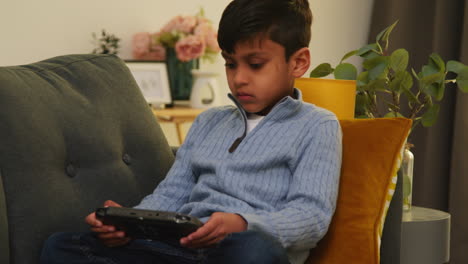 young boy sitting on sofa at home playing game or streaming onto handheld gaming device 2