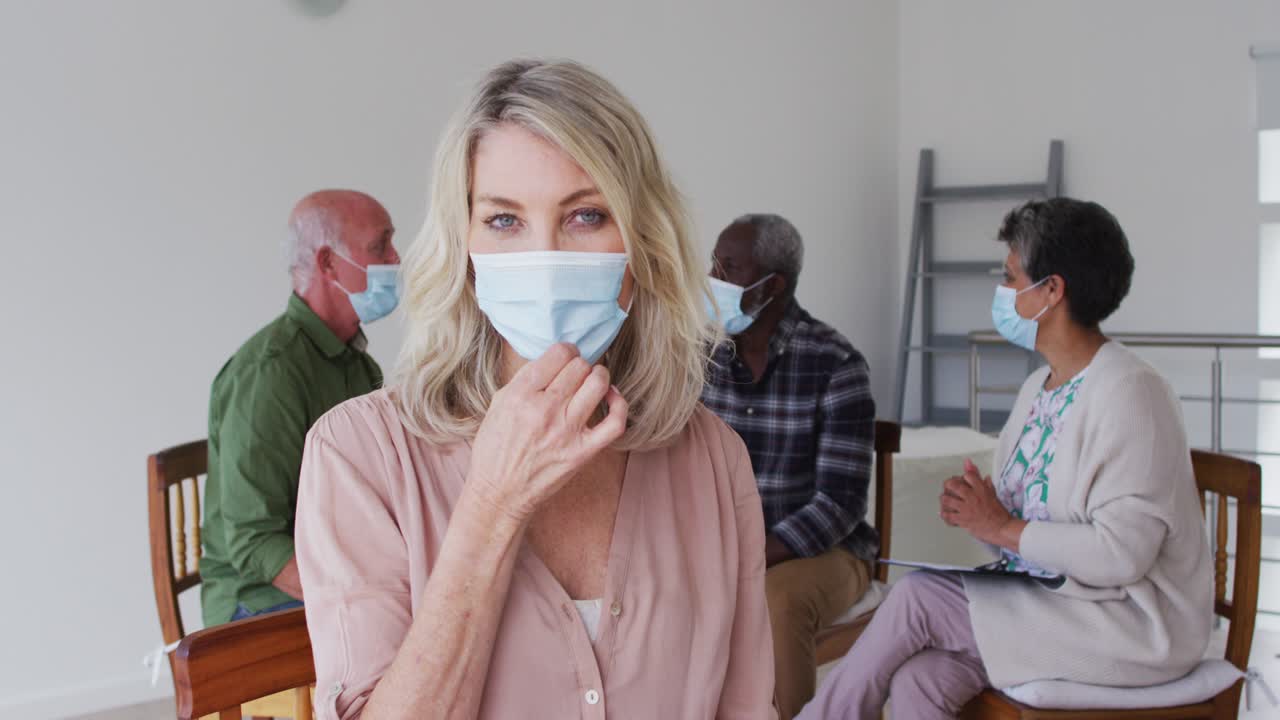 두 명의 다양한 노인 커플이 원에 앉아서 집에서 치료 대화를 나누고 카메라를 보고 있습니다.