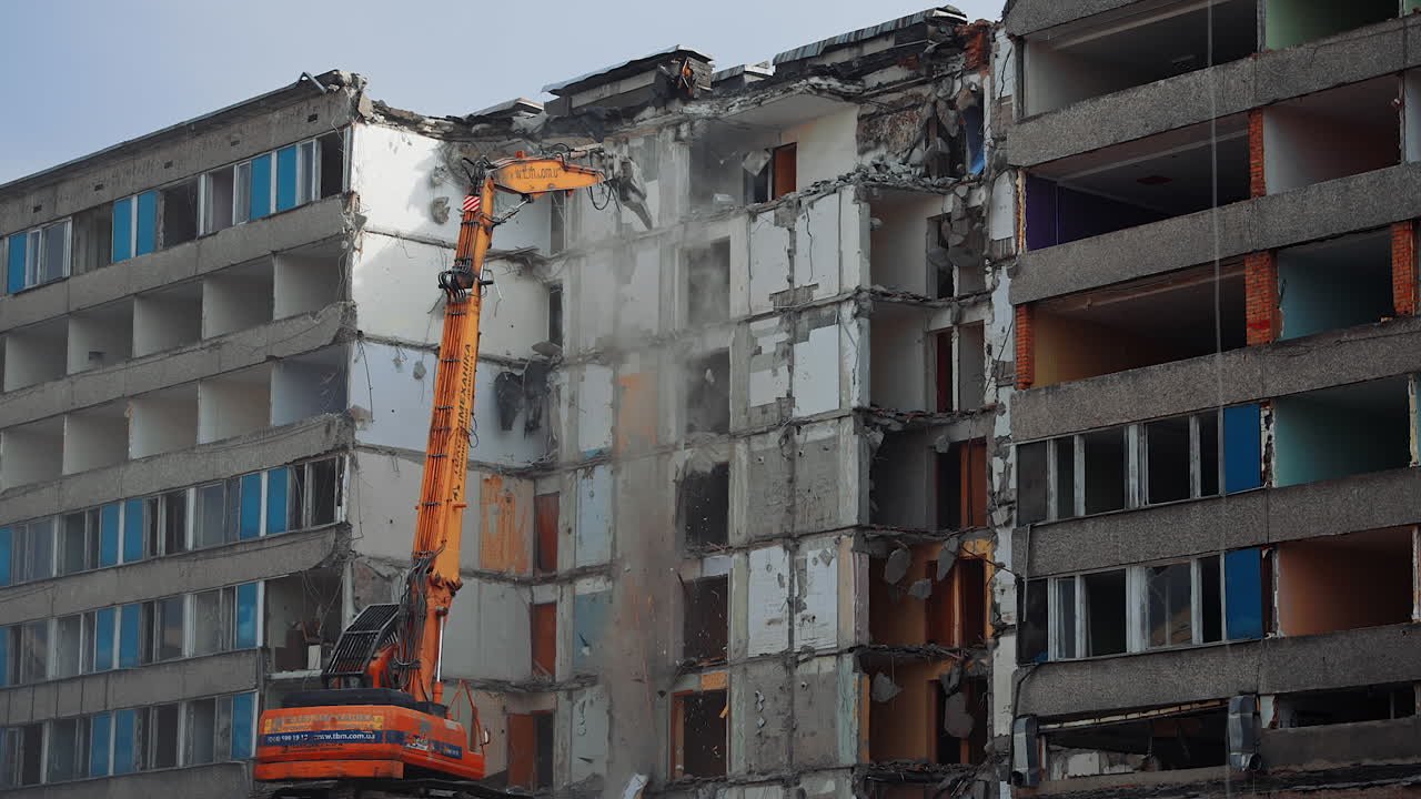Powerful excavator tears off the pieces of destroyed house and throws them down. Demolition of a large building ruined by an earthquake.