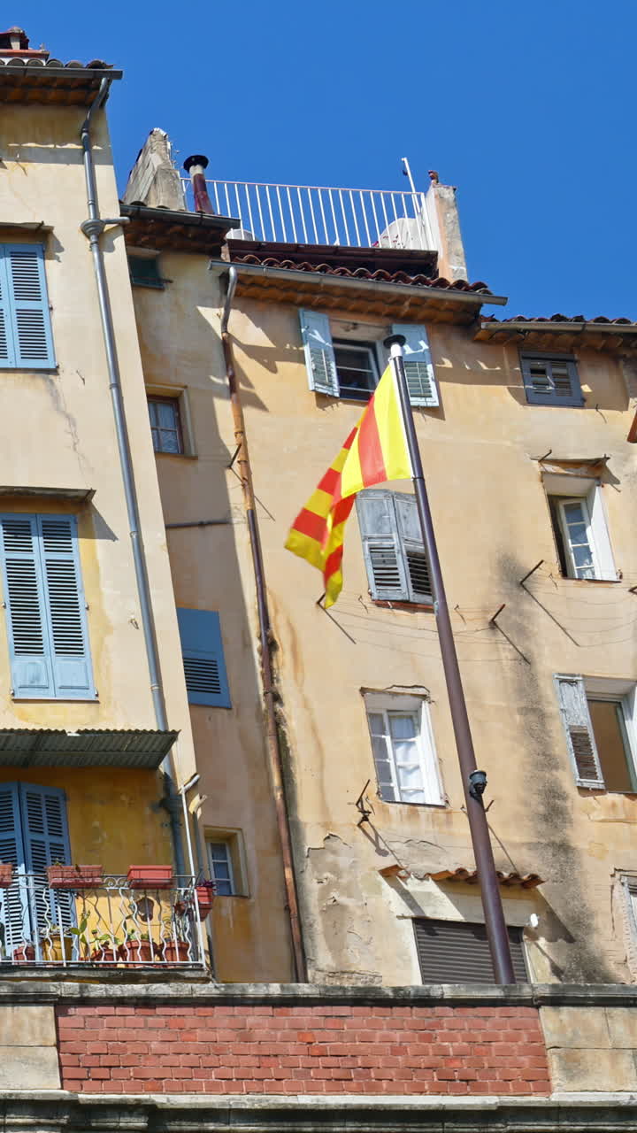 View of a yellow and red striped flag near the old buildings in Grasse, France. Vertical