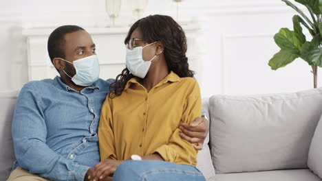 Retrato-De-Una-Pareja-Joven-Con-Máscaras-Médicas-Sentada-En-El-Sofá-En-Casa