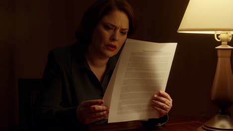 woman reads a document under a lamp with a concerned expression