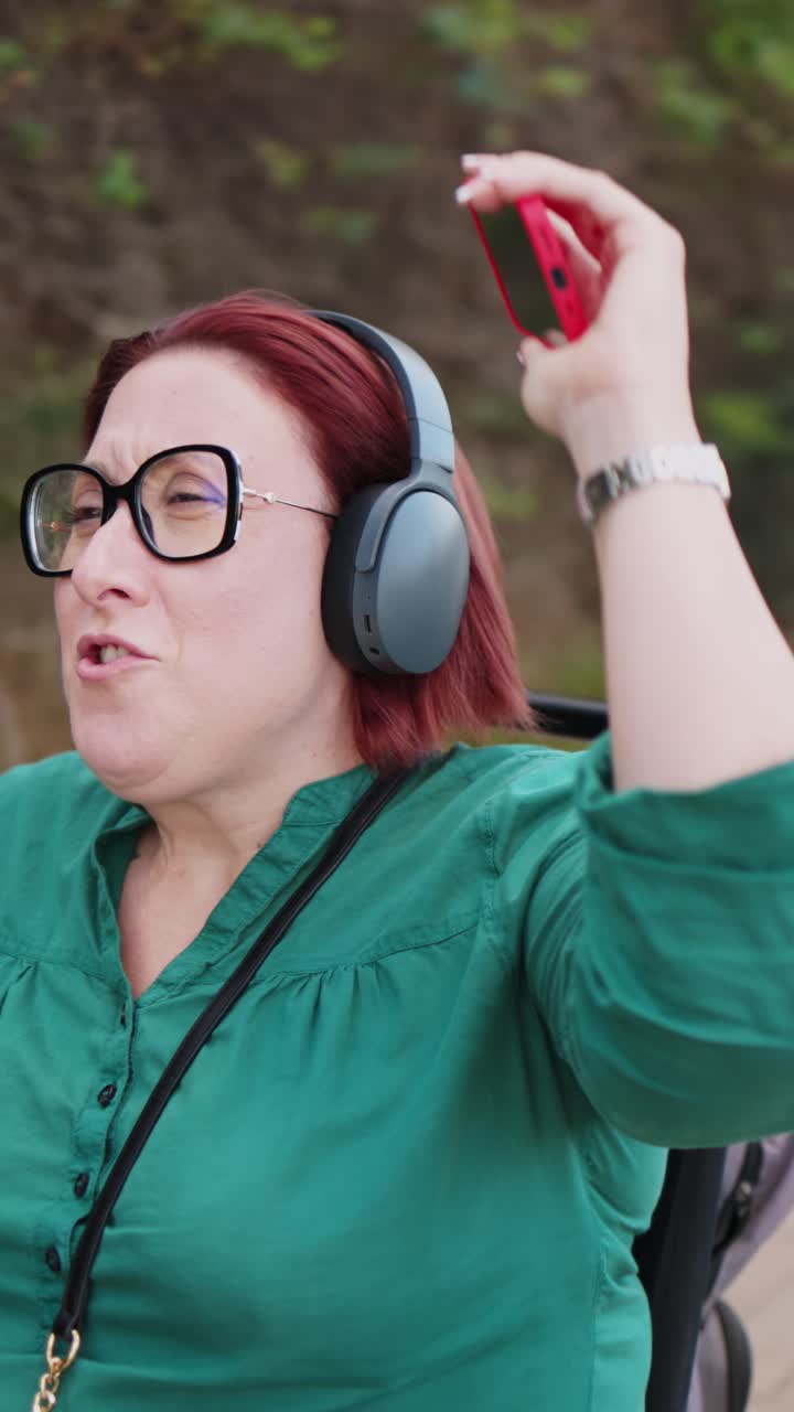 Donna felice in sedia a rotelle elettrica che ascolta musica sullo smartphone.