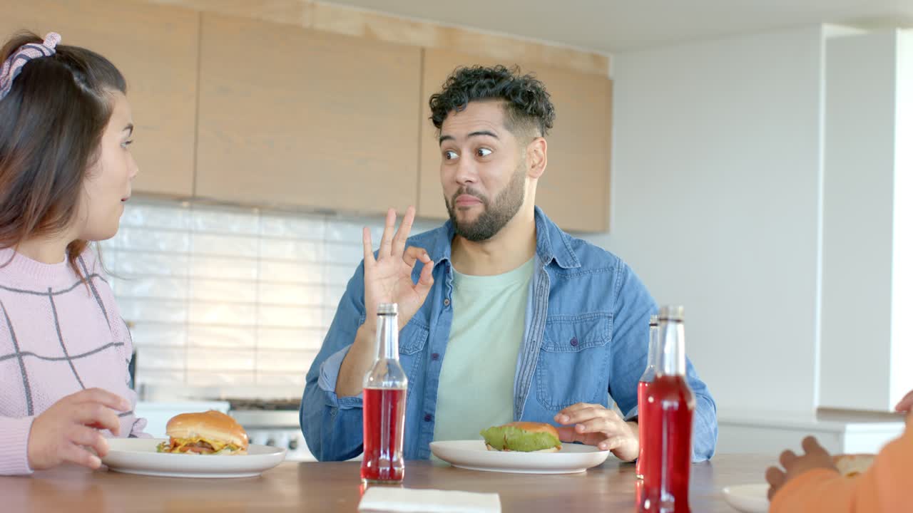 Amigos probando una hamburguesa con pan verde para el sabor y bebiendo refresco en la isla de la cocina, intercambiando opiniones.