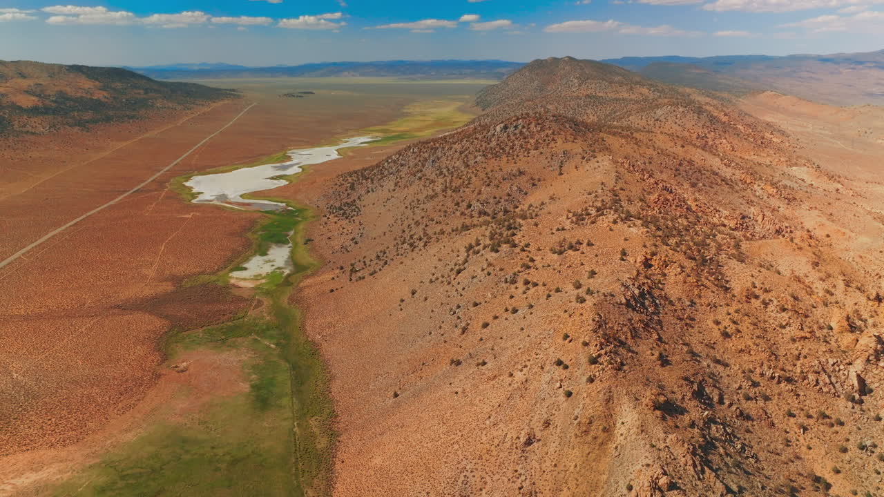 Dry sandy landscape of Nevada, United States on sunny day. Rocky hills with some puddles surrounded by scarce greenery from top view.