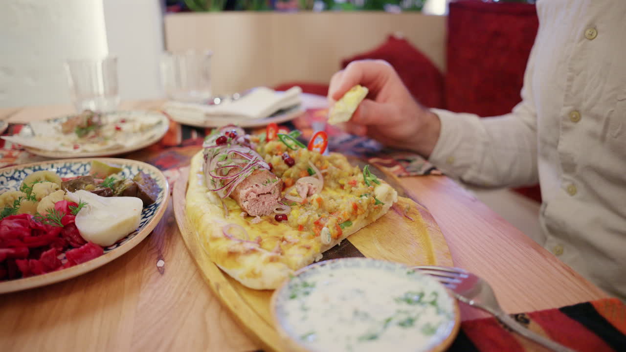 Primer plano de una mujer cortando carne a la parrilla sobre pan plano, servida con salsa cremosa y verduras