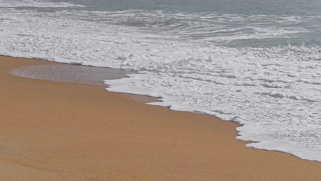 SLOW-MOTION-waves-white-with-foam-cover-the-wet-sand-of-the-beach,-Portugal