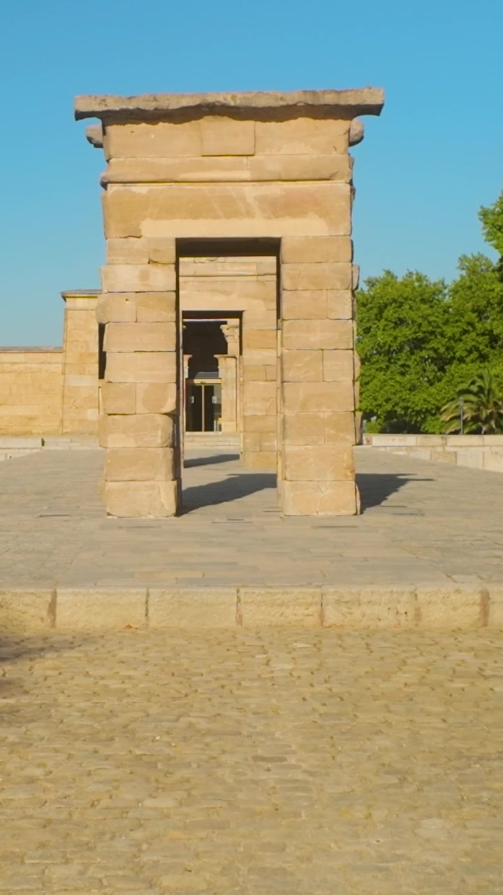 Una perspectiva vertical del antiguo Templo egipcio de Debod en Madrid, España. Este monumento histórico es capturado durante la hora dorada, mostrando auténtica arquitectura de piedra y cielos azules despejados