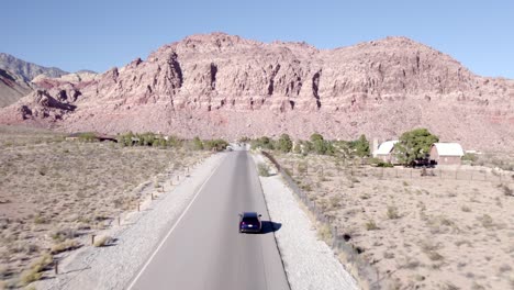 Disparo-De-Un-Dron-Rastreando-Un-Auto-Conduciendo-A-Través-Del-Cañón-De-Roca-Roja-En-Nevada,-América