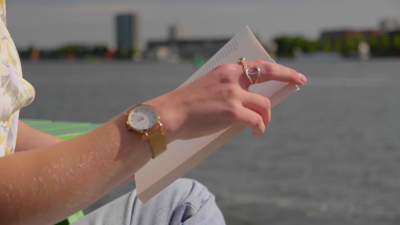 стильная женщина читает книгу, сидя на пирсе под теплым солнцем