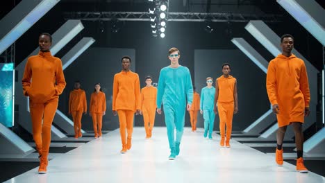 a dynamic fashion showcase featuring models in vibrant orange and blue outfits strutting down a modern runway with high-tech stage aesthetics