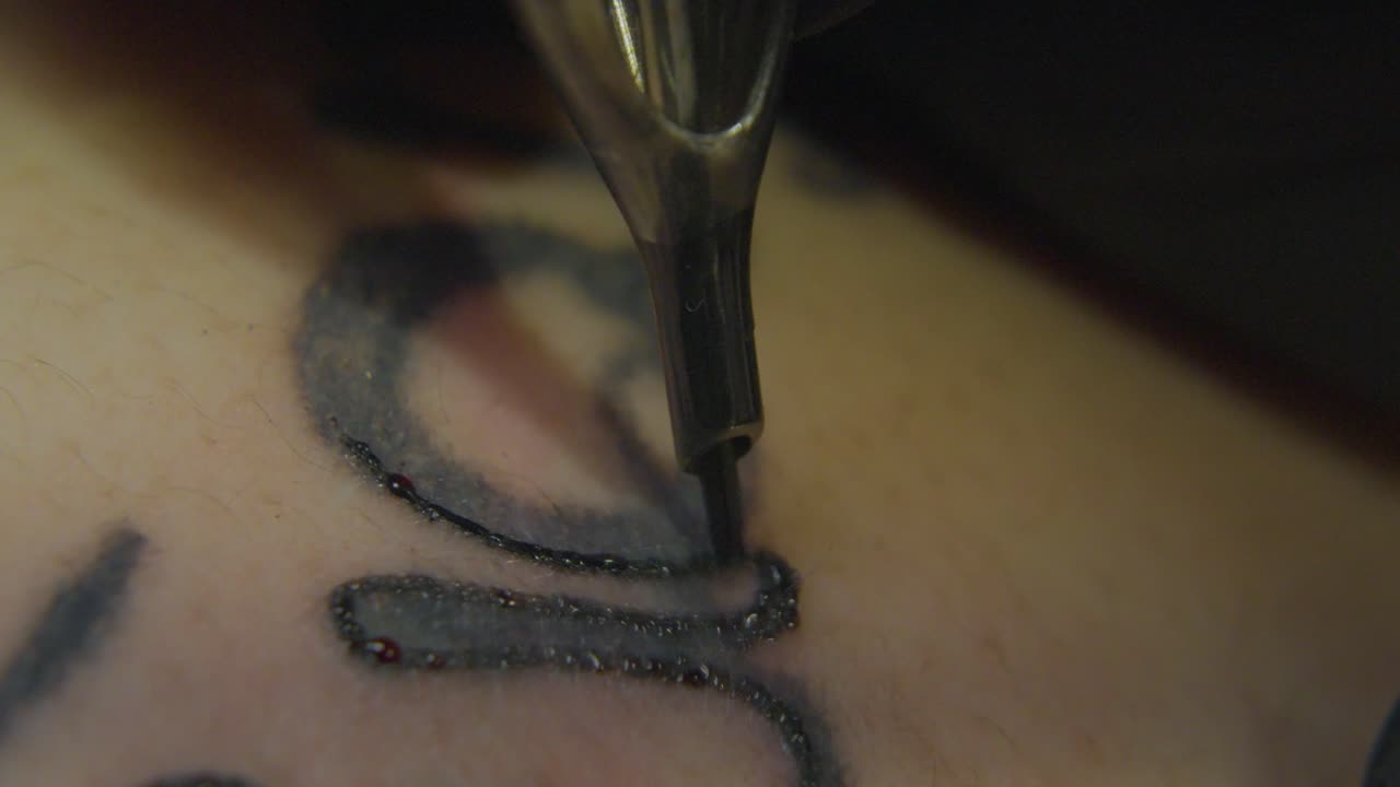 una aguja de tatuaje que se mueve rápidamente tinta el contorno de una obra de arte existente causando gotas de sangre para formarse en la superficie de la piel