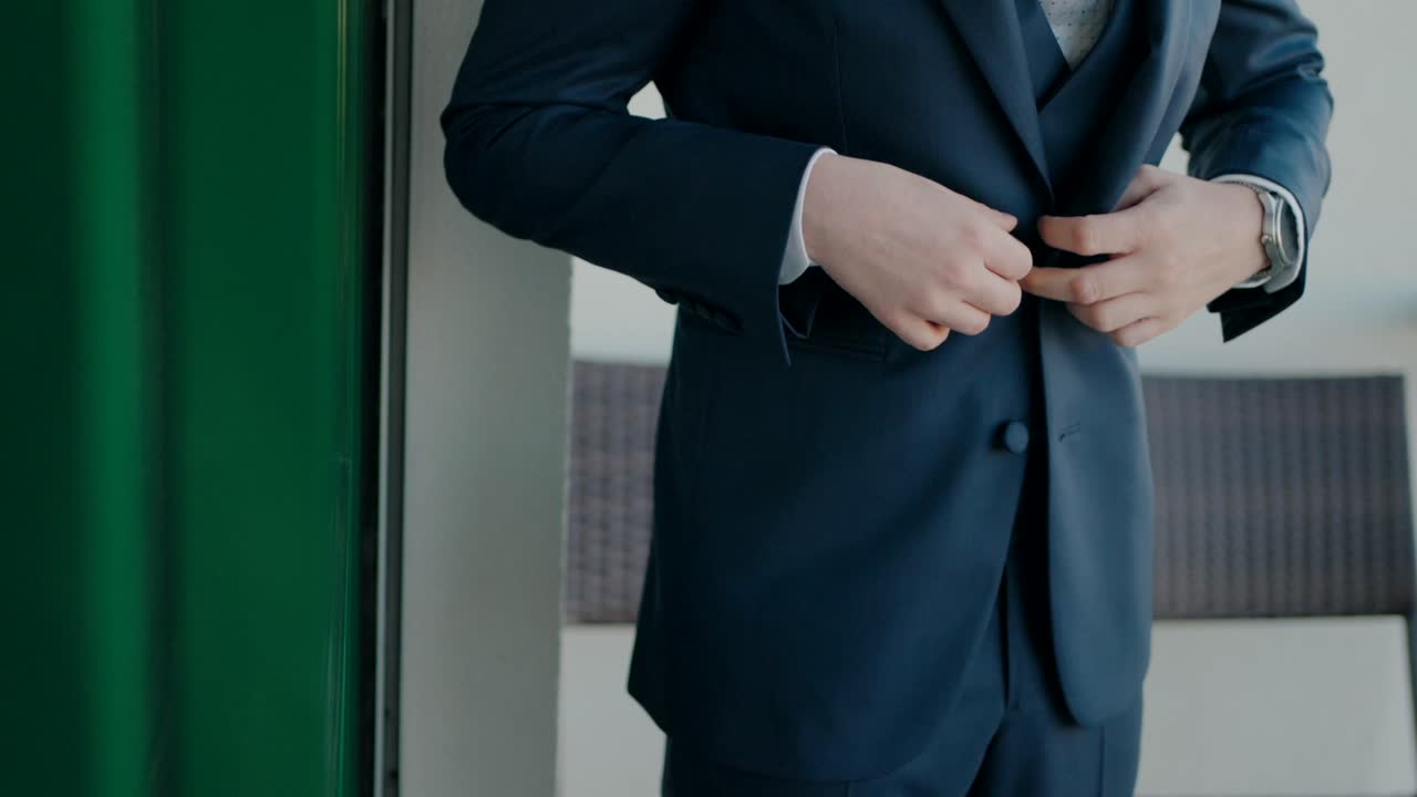 Man in a dark blue suit adjusting his jacket button with a silver watch visible