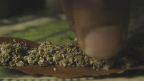 close up of a black mans finger lining up the ground cannabis bud to prepare to roll a blunt of marijuana