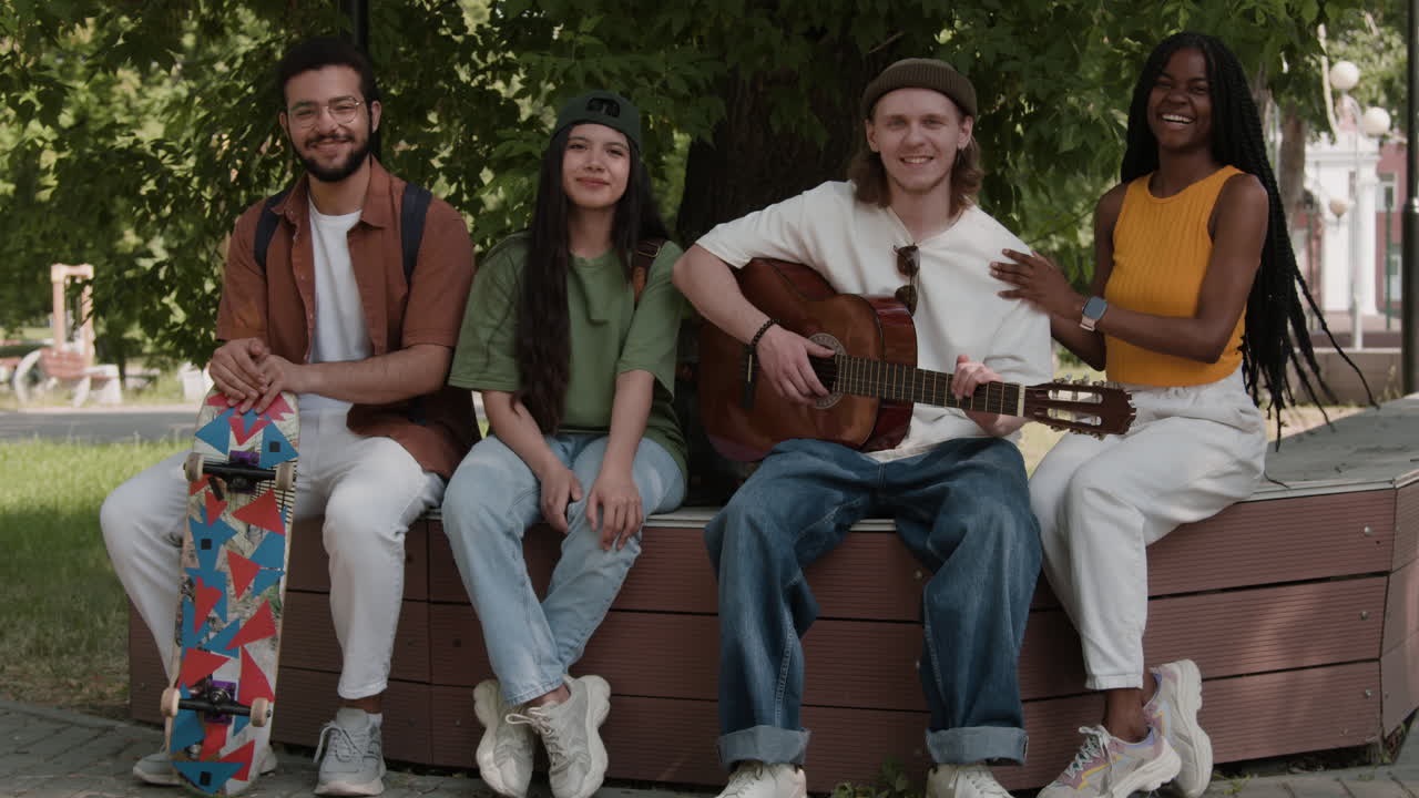 Diverse group of young friends relaxing in a park, playing guitar and socializing