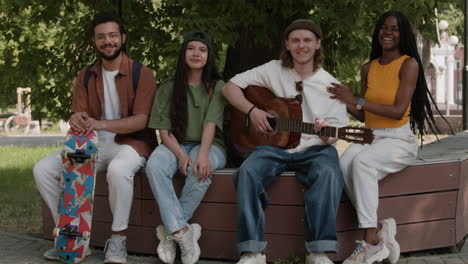 diverse group of young friends relaxing in a park, playing guitar and socializing