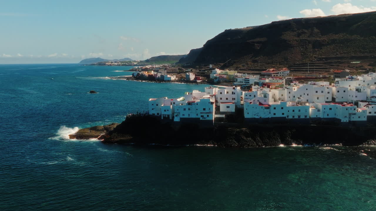 Aerial: Atlantic Ocean with blue color and white neighborhood during the day in Gran Canaria, Spain, pan drone shot