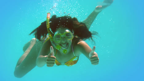 una morena feliz con un snorkel bajo el agua mostrando los pulgares hacia arriba