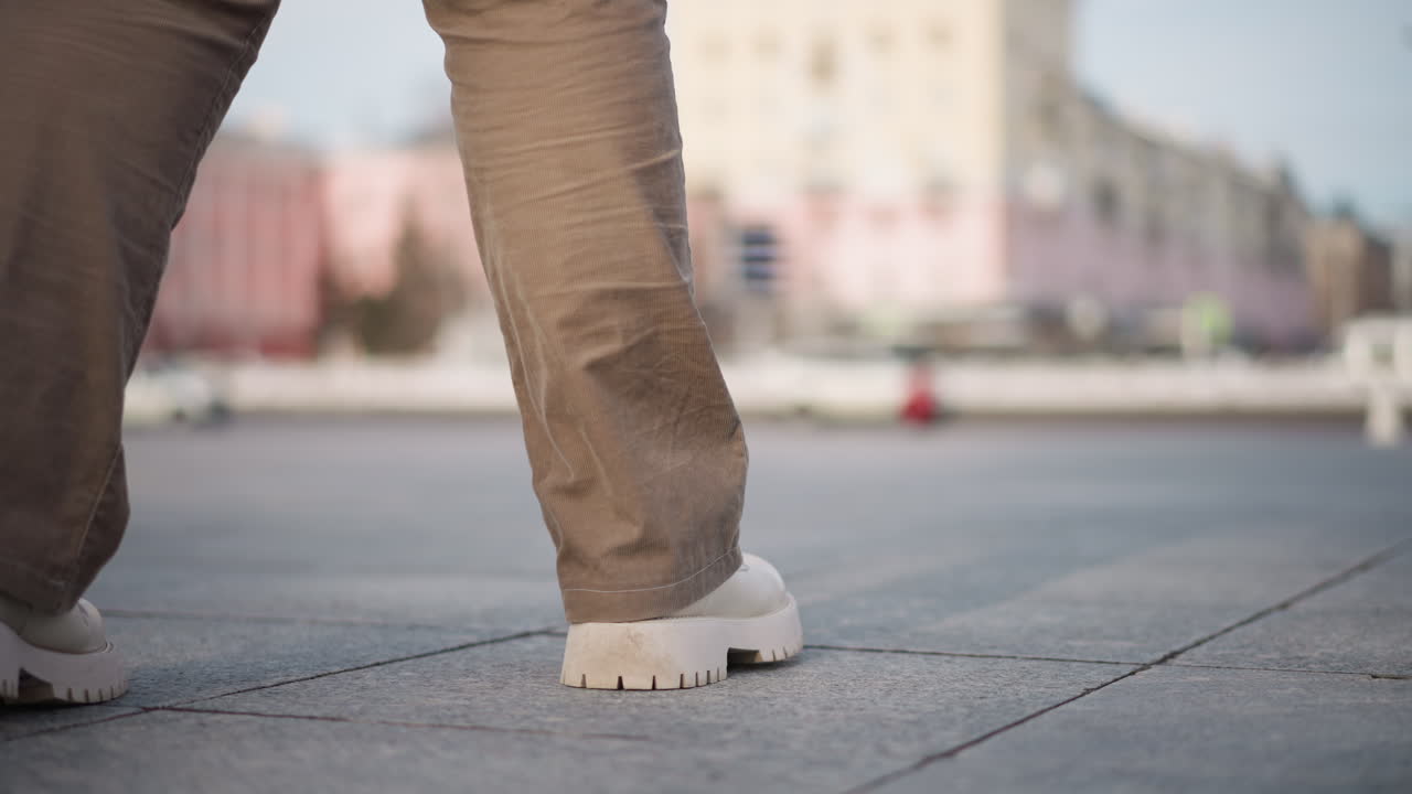 Back view of dancer legs making rhythmic moves while performing choreography on outdoor tiled pavement under winter light capturing dynamic motion and energy against urban snowy street backdrop