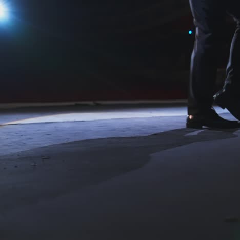 actor's legs dancing on stage. man in black shoes dancing against the theatre hall at dark scenic light. close-up.