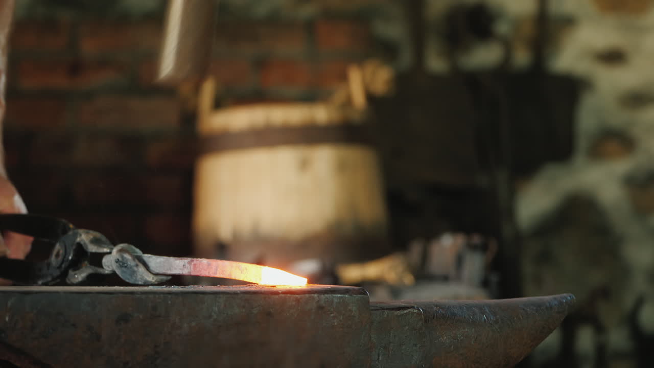 un herrero trabaja en una fragua un primer plano del yunque y el tocho al rojo vivo en el que el martillo bea