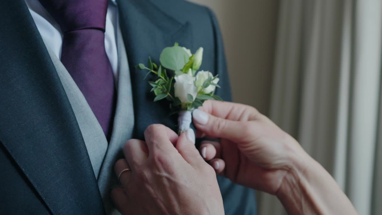 Close up of hands adjusting the groom’s floral boutonniere on a formal suit