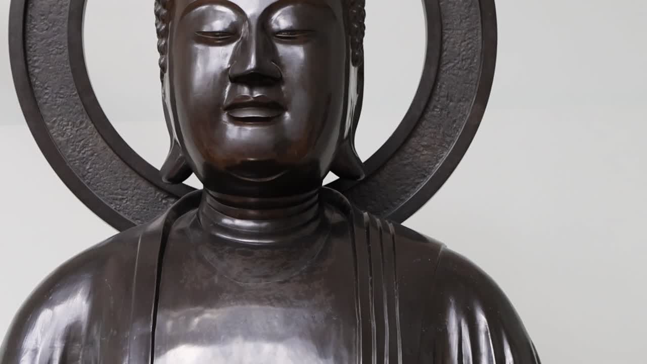 Detailed view of a bronze Buddha statue's upper body and halo, highlighting serene expression and craftsmanship.